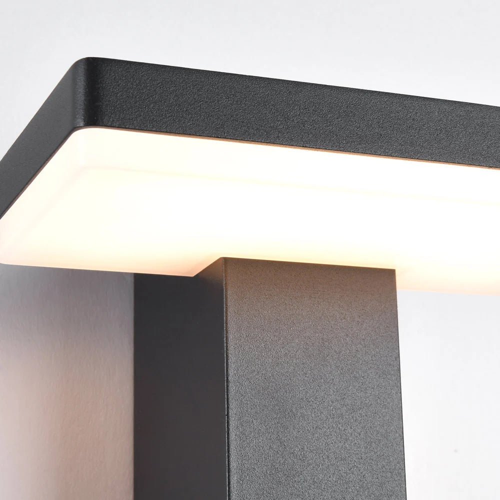 Detail schuin van onderen van de brandende zwarte wandlamp Robert zonder sensoren op de afeelding is het strakkelijnenspe van de buitenverlichting wandlamp goed zichtbaar