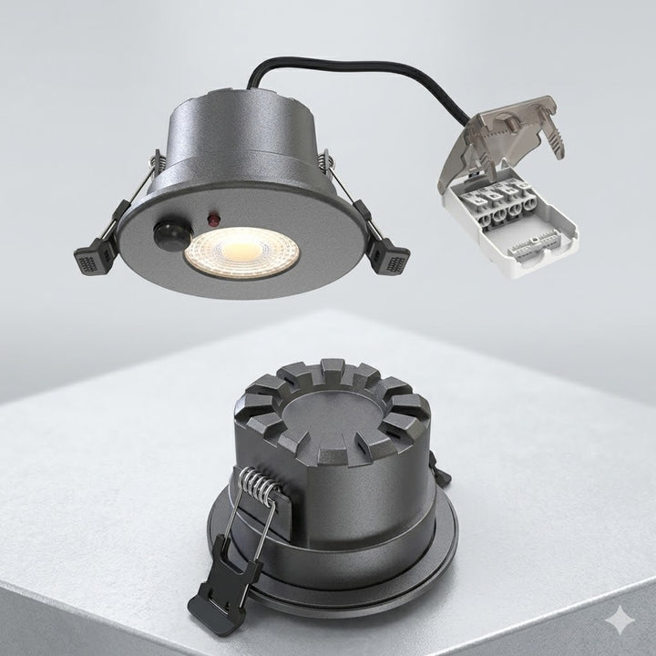 Twee aanzichten van een zwarte LED inbouwspot met bewegingssensor. De bovenste spot zweeft en toont de lichtbron, de sensor en de aangesloten klemmenstrookmet open geklapte beschermkap. De onderste spot staat op een oppervlak en toont de koelvinnen en de veerklemmen voor montage.